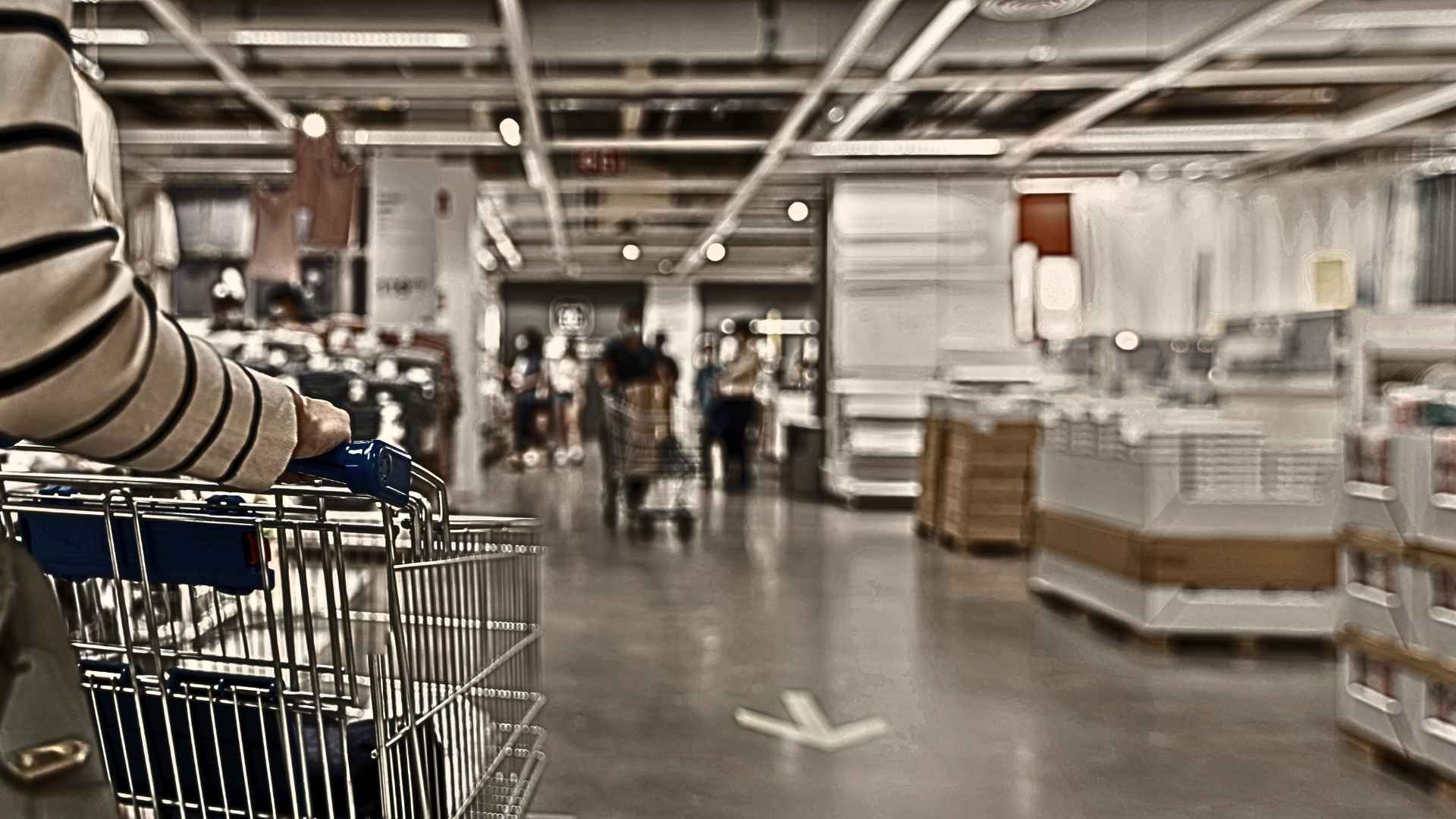 The image shows a shopping cart in the foreground that appears to being pushed in what appears to be an IKEA warehouse.